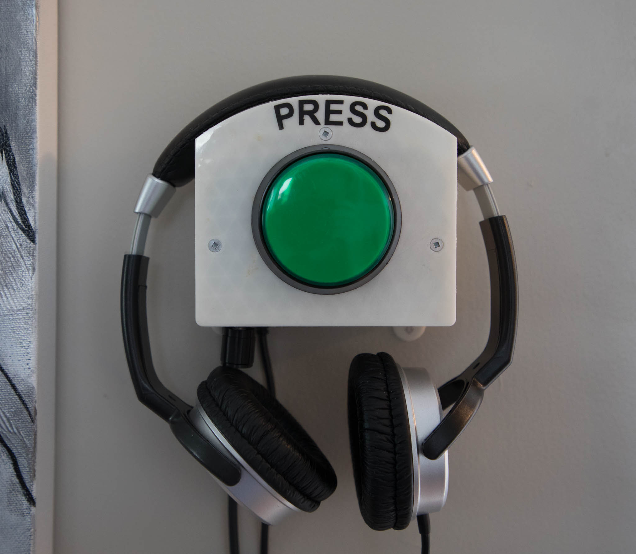Picture of headset to be used in upcoming show for accessibility. It is a white box with a large green button, with headphones hanging on it