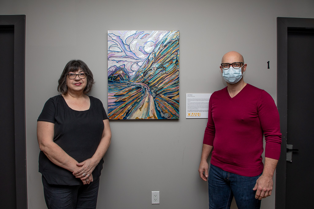 Robyn Rennie (left side) and Chad Watters standing beside a painting called north Shore